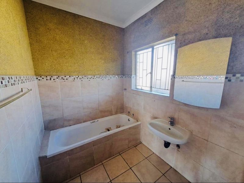 A dated bathroom featuring a built-in bathtub, wall-mounted basin, and tiled finishes, currently requiring maintenance and cosmetic updates to modernize the space.