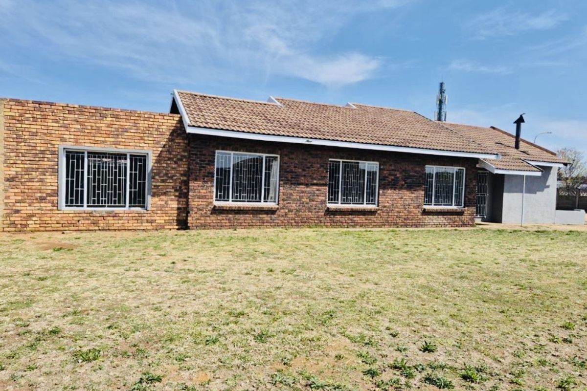 A rear view of a single-story face-brick house featuring a tiled roof and security-barred windows, set against a large open lawn area.