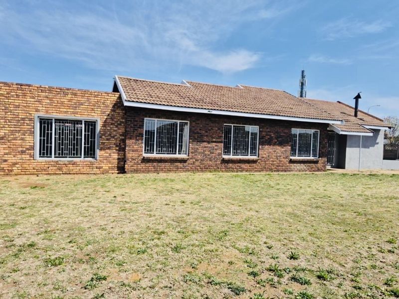 A rear view of a single-story face-brick house featuring a tiled roof and security-barred windows, set against a large open lawn area.