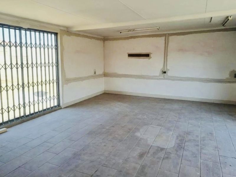 An empty, unfinished garage space featuring tiled flooring, a security gate, and exposed wall plaster, offering potential for renovation or storage use.