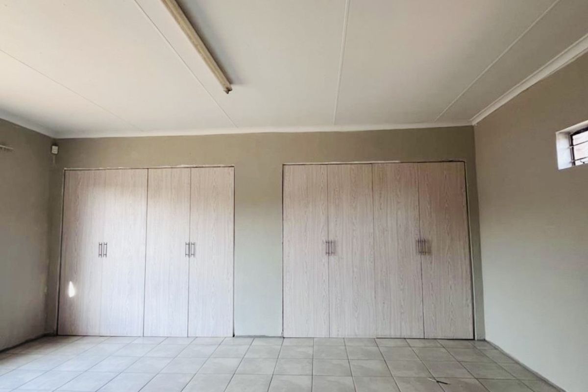 A spacious, empty bedroom featuring neutral tiled flooring and extensive built-in cupboard storage, offering a blank canvas for personalization.