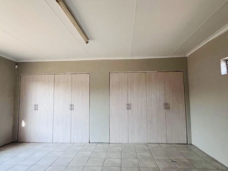A spacious, empty bedroom featuring neutral tiled flooring and extensive built-in cupboard storage, offering a blank canvas for personalization.