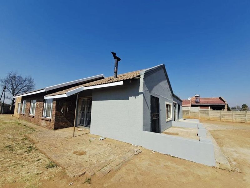 Rear exterior view of a single-story house featuring a combination of brick and painted walls, a tiled roof, and a paved patio area.