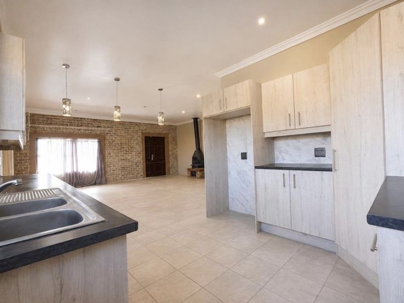Spacious open-plan living and kitchen area featuring light wood cabinetry, a double sink, exposed brick accents, and a modern freestanding fireplace.