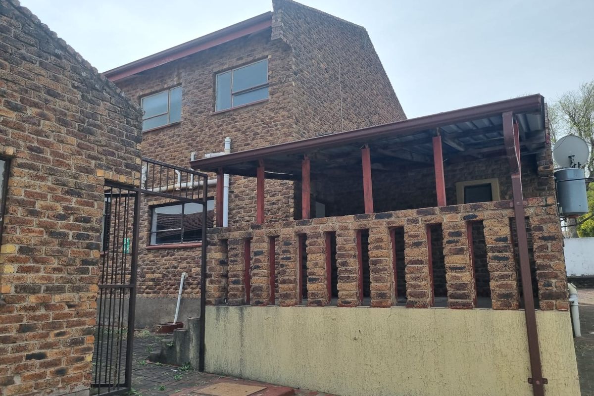 Rear view of a double-story face brick house featuring a covered patio area with a brick balustrade and paved courtyard.