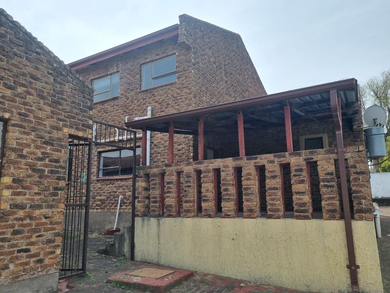 Rear view of a double-story face brick house featuring a covered patio area with a brick balustrade and paved courtyard.