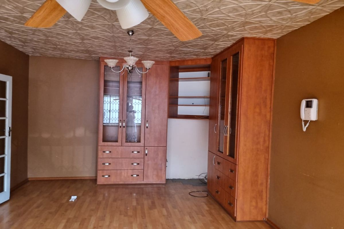 Spacious living area featuring built-in wooden cabinetry, decorative ceiling tiles, a ceiling fan, and laminate flooring, providing a functional and versatile space.