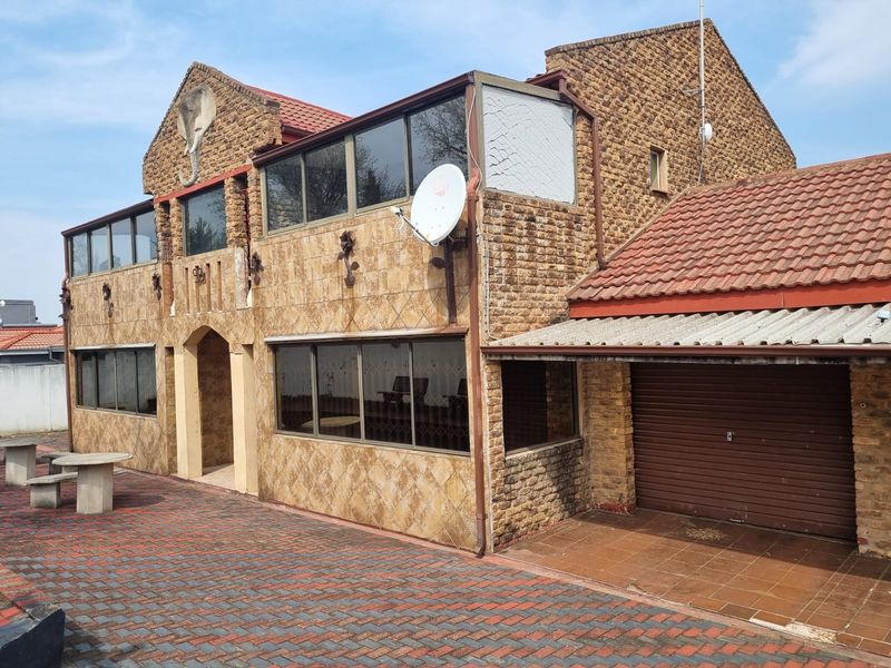 Front elevation of a multi-story brick house featuring a tiled roof, integrated garage with roller shutter door, and paved driveway area.