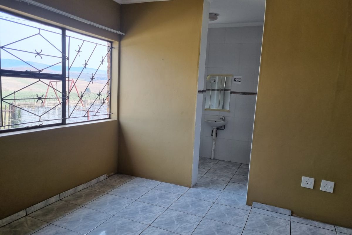 An empty bedroom featuring tiled flooring, security bars on the window, and an attached en-suite bathroom with a wall-mounted basin.