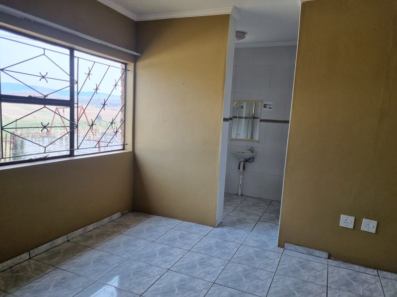 An empty bedroom featuring tiled flooring, security bars on the window, and an attached en-suite bathroom with a wall-mounted basin.