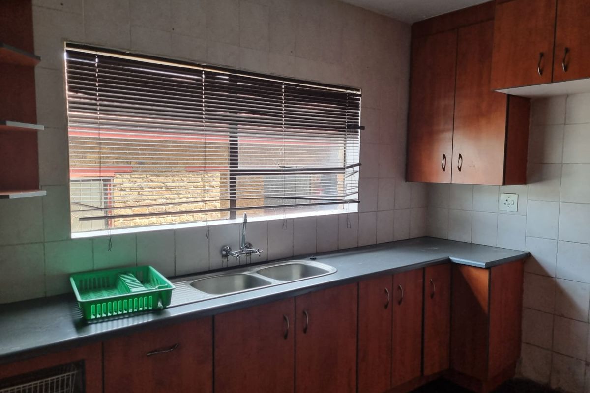 A functional kitchen featuring wooden cabinetry, a double bowl stainless steel sink, and tiled splashbacks, offering a blank canvas for modern updates.