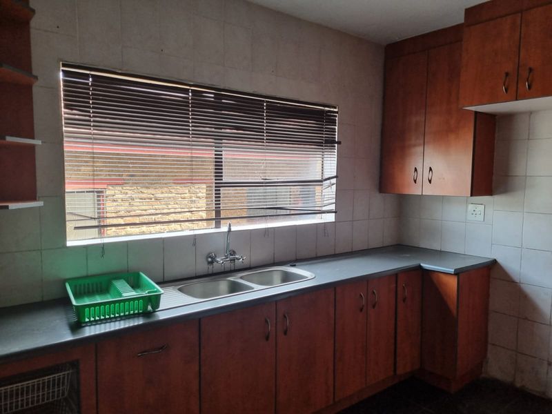 A functional kitchen featuring wooden cabinetry, a double bowl stainless steel sink, and tiled splashbacks, offering a blank canvas for modern updates.