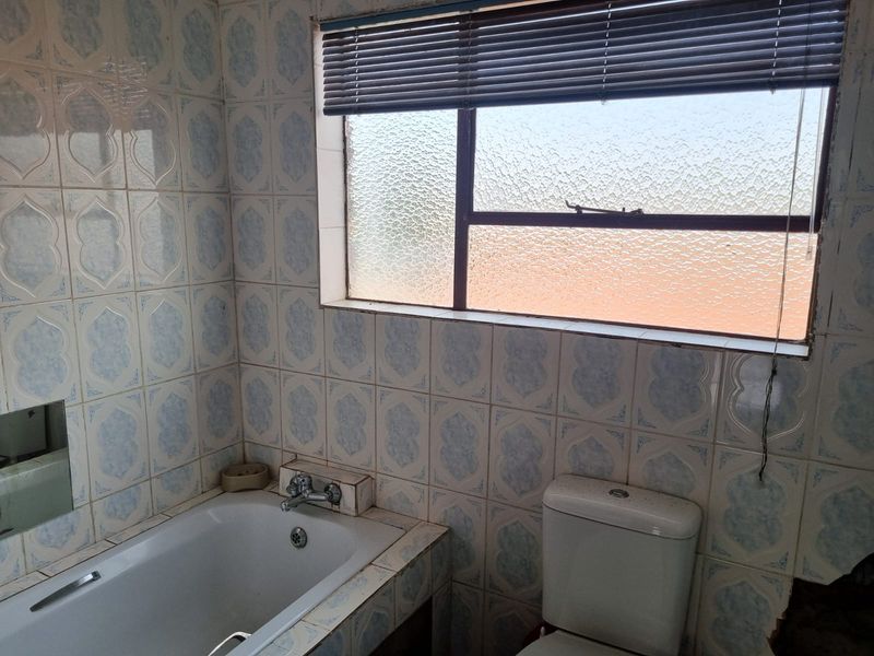A dated bathroom featuring a built-in bathtub, toilet, and patterned ceramic wall tiles with an obscured glass window.