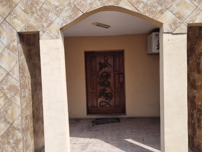 Front entrance featuring an arched porch, decorative carved wooden door, and tiled facade with integrated air conditioning unit.
