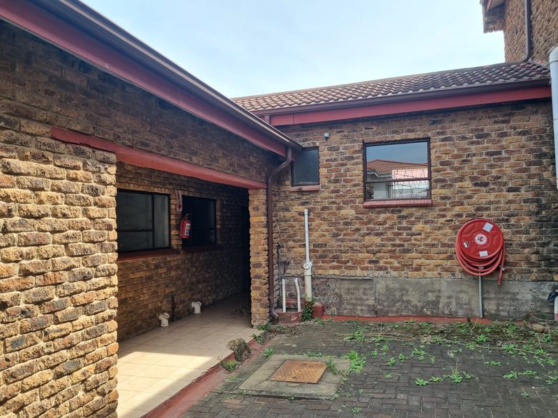 A rear exterior view of the property featuring face brick walls, a tiled roof, a paved courtyard area, and installed fire safety equipment.