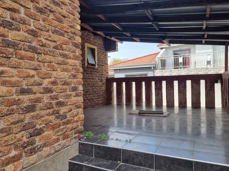 A covered outdoor patio area featuring exposed brick walls, tiled flooring, and a balustrade, offering a functional space for outdoor relaxation.