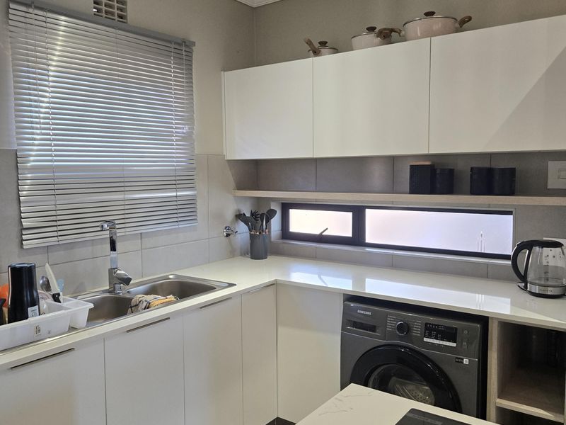 Modern kitchen featuring sleek white cabinetry, quartz countertops, integrated induction hob, stainless steel sink, and contemporary tiled splashback with recessed lighting.