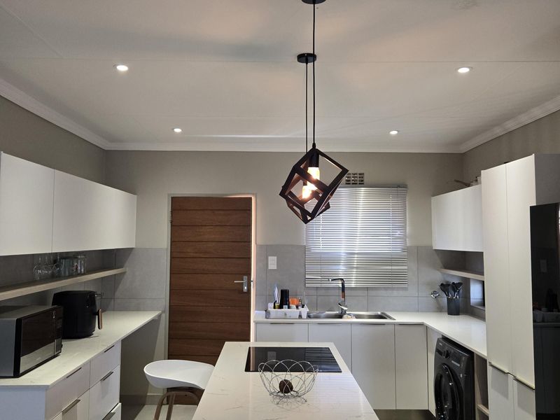 Modern kitchen featuring a central island with quartz countertops, built-in hob, integrated appliances, sleek white cabinetry, and contemporary pendant lighting.