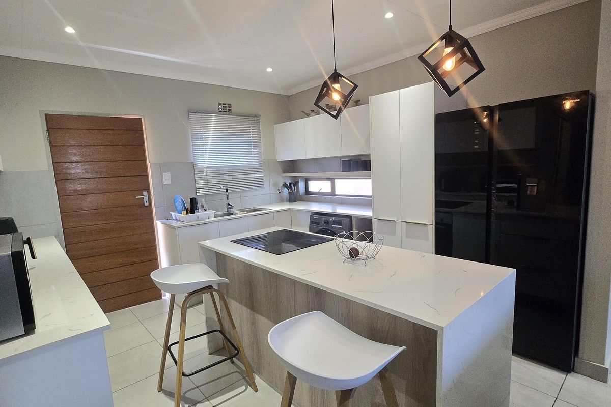 Modern kitchen featuring a central island with quartz countertops, sleek cabinetry, integrated hob, and contemporary pendant lighting, finished with neutral tiled flooring.