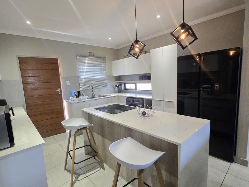 Modern kitchen featuring a central island with quartz countertops, sleek cabinetry, integrated hob, and contemporary pendant lighting, finished with neutral tiled flooring.
