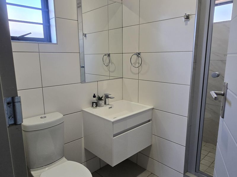 A modern, compact bathroom featuring a wall-mounted vanity, white tiled walls, and a separate shower enclosure.