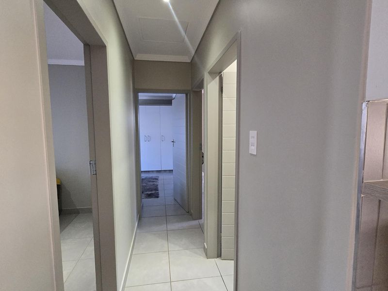 A clean, well-lit hallway featuring neutral tiled flooring and recessed ceiling lighting, providing access to multiple rooms.