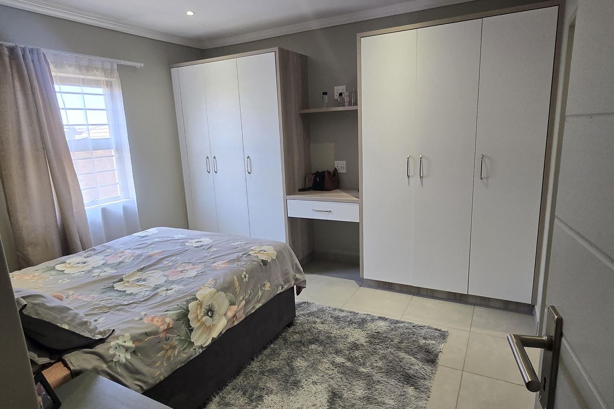 A well-maintained bedroom featuring neutral tiled flooring, built-in cupboards with an integrated vanity station, and recessed ceiling lighting.