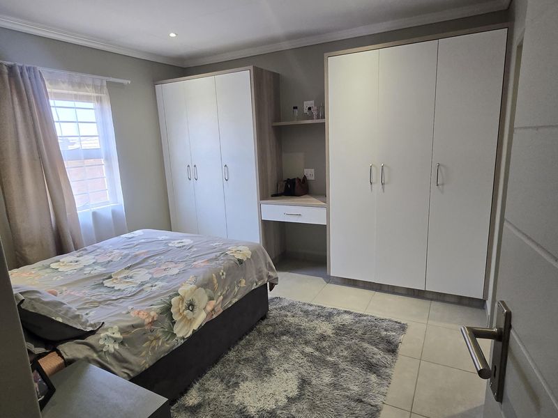 A well-maintained bedroom featuring neutral tiled flooring, built-in cupboards with an integrated vanity station, and recessed ceiling lighting.
