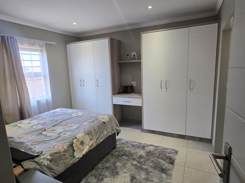 A well-maintained bedroom featuring neutral tiled flooring, recessed ceiling lighting, and extensive built-in cabinetry with an integrated vanity area.