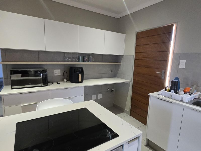 Modern kitchen featuring white cabinetry, stone countertops, a central island with an integrated electric hob and oven, and tiled flooring.