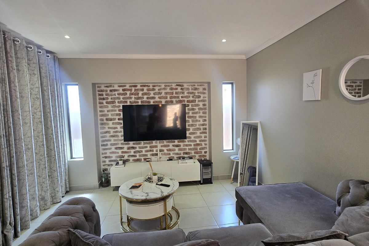 A well-maintained living room featuring a distinctive exposed brick feature wall, tiled flooring, and recessed downlighting, creating a modern and inviting atmosphere.