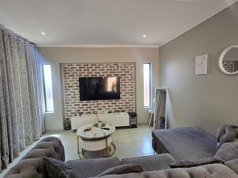 A well-maintained living room featuring a distinctive exposed brick feature wall, tiled flooring, and recessed downlighting, creating a modern and inviting atmosphere.