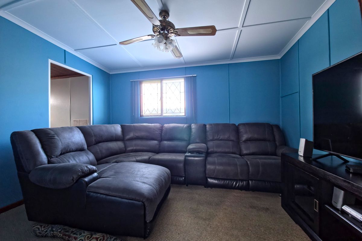 A living room featuring a ceiling fan and a window with security bars, finished with blue wall paneling.