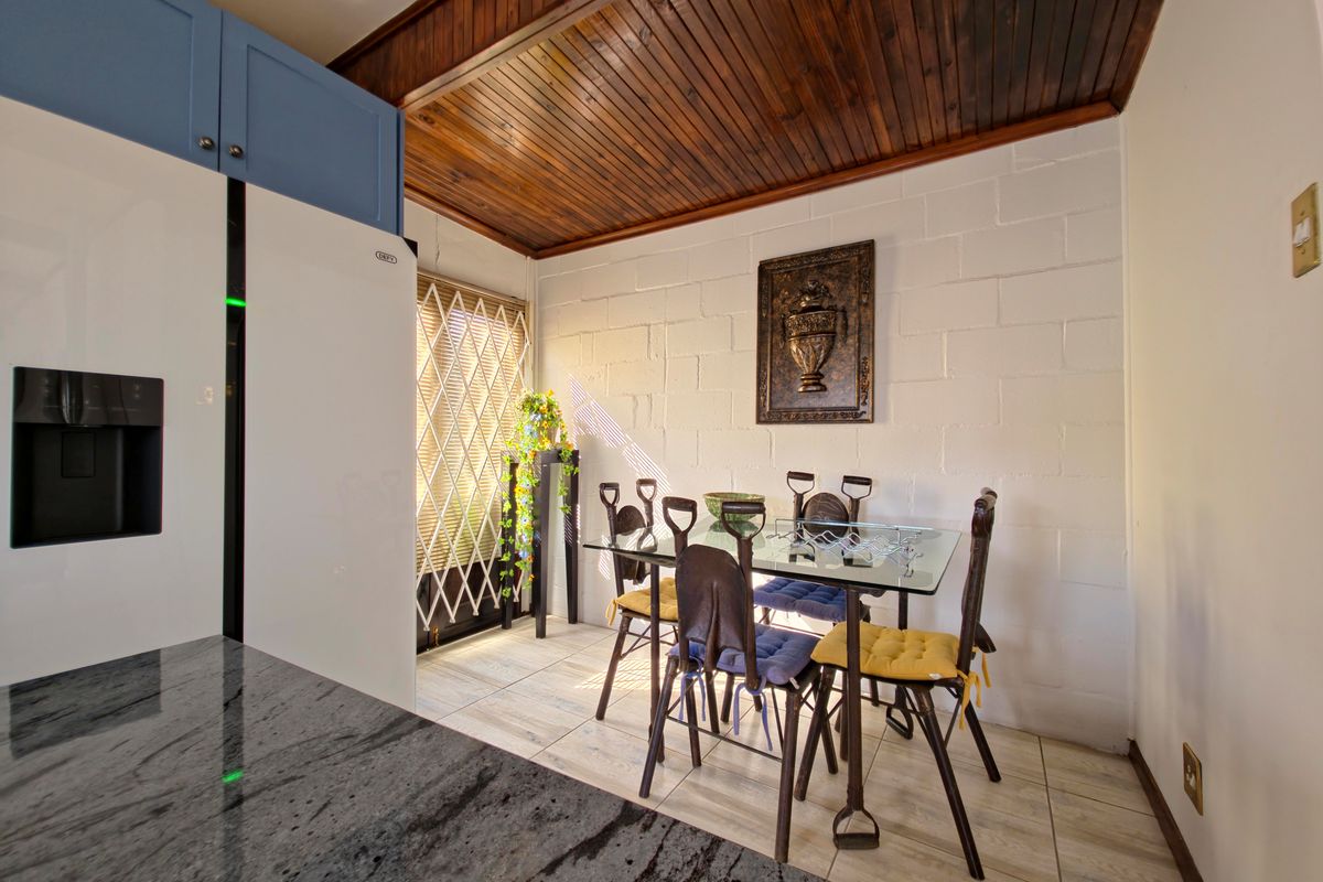 A kitchen dining area featuring a granite countertop, built-in cabinetry, and a distinctive timber tongue and groove ceiling with tiled flooring.