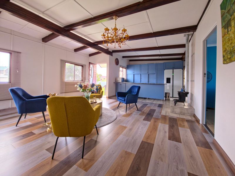 Spacious open-plan living area featuring exposed timber ceiling beams, modern laminate flooring, a wood-burning stove, and integrated kitchen cabinetry.