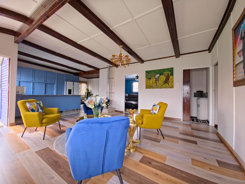 Spacious open-plan living area featuring exposed timber ceiling beams, laminate flooring, a wood-burning fireplace, and an integrated kitchen with blue cabinetry.