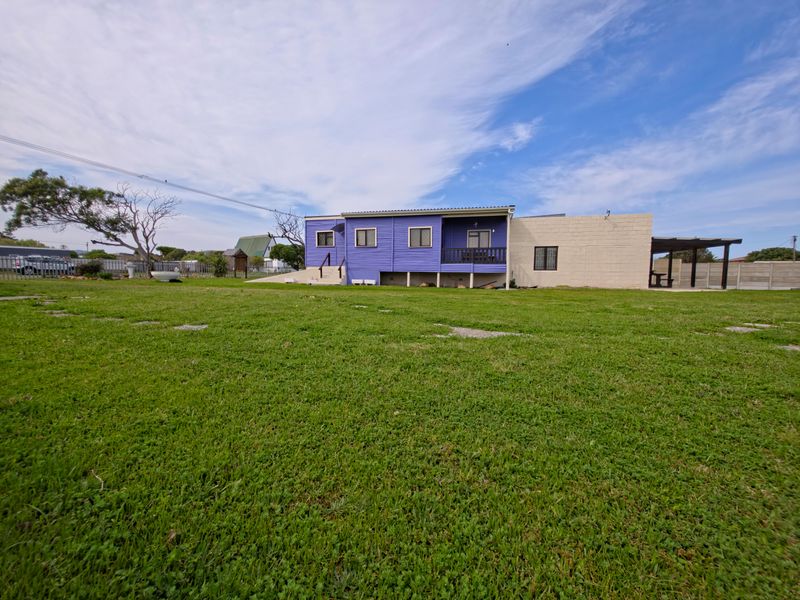 A rear view of the property featuring a purple corrugated metal facade, a concrete block extension, and a spacious grass lawn.