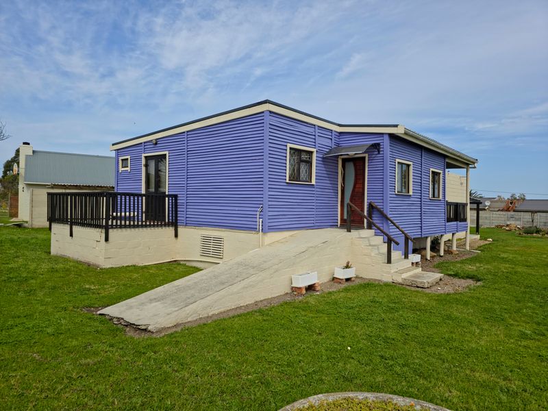 Exterior view of a purple timber-clad house featuring a concrete access ramp, stairs, and a raised timber deck.