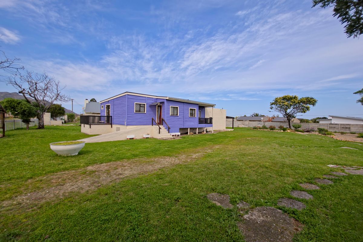 Rear view of a detached house featuring a raised timber deck, concrete access ramp, and corrugated metal siding set within a large garden area.