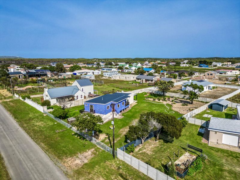Aerial view of a residential property featuring a blue house, surrounding garden, and perimeter fencing within a coastal neighborhood setting.