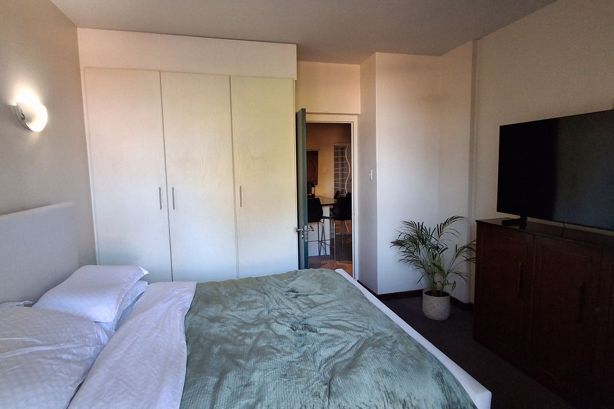 A bedroom featuring built-in wardrobes and a wall-mounted light fixture, with an adjacent doorway leading to another living space.