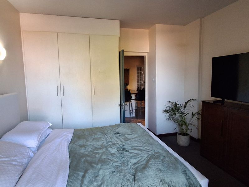 A bedroom featuring built-in wardrobes and a wall-mounted light fixture, with an adjacent doorway leading to another living space.