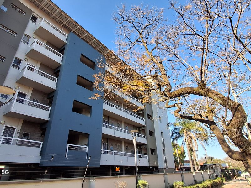 Exterior view of a modern multi-story apartment building featuring private balconies with metal railings and secure perimeter walling with electric fencing.