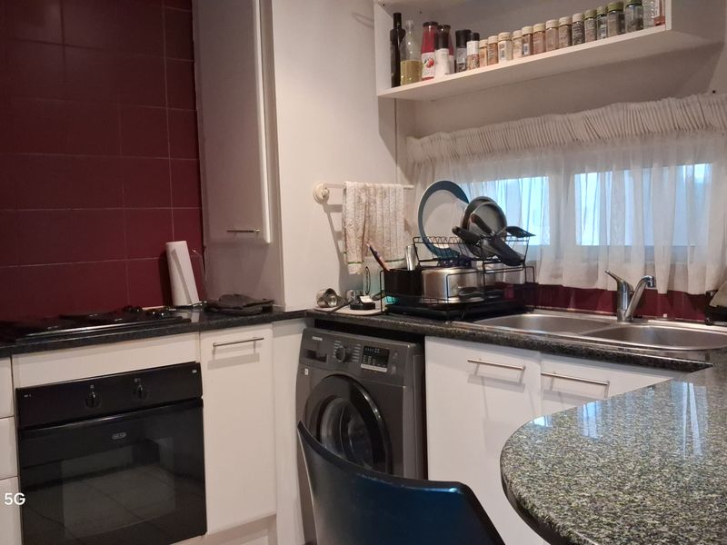 Compact kitchen featuring granite countertops, built-in oven, hob, and double basin sink with tiled splashback and overhead storage shelving.