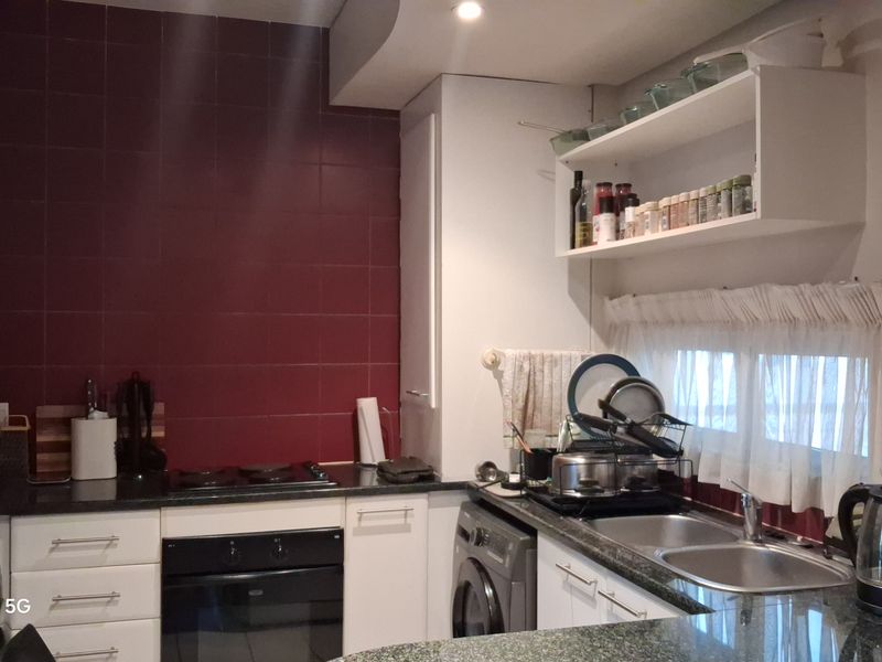 A functional kitchen featuring dark granite countertops, a tiled backsplash, built-in oven and hob, and integrated laundry appliances.