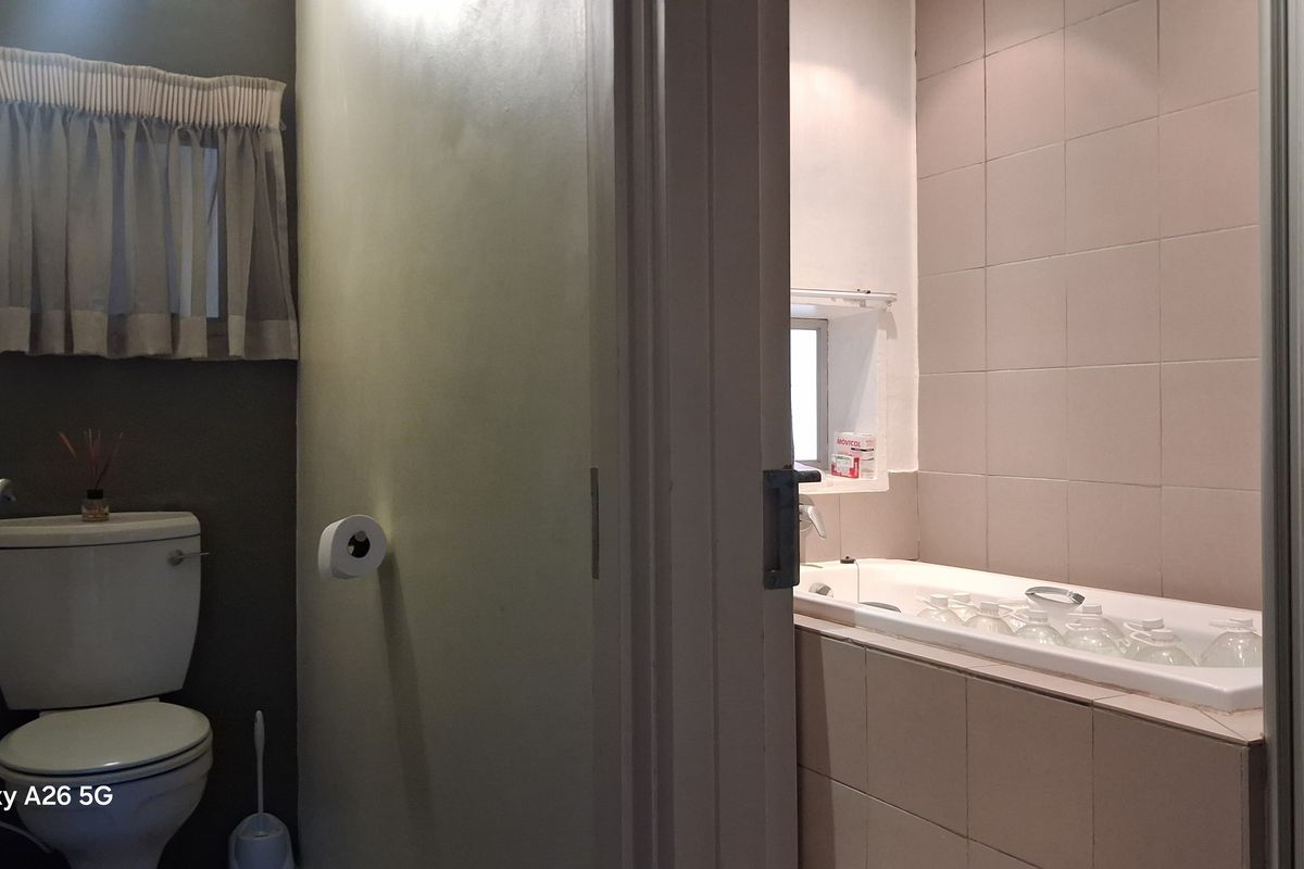 A functional bathroom featuring a built-in bathtub with tiled surround and a separate toilet area with neutral wall finishes.