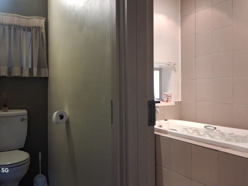 A functional bathroom featuring a built-in bathtub with tiled surround and a separate toilet area with neutral wall finishes.