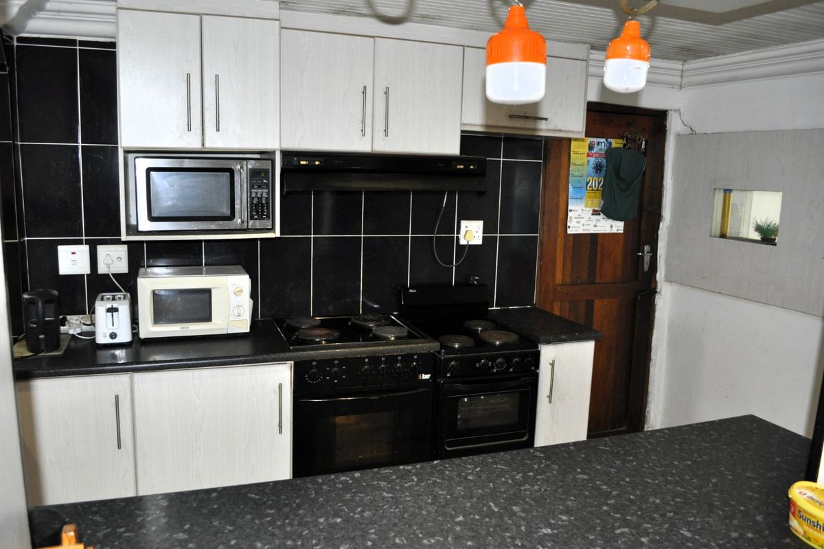 Functional kitchen featuring black tiled backsplash, laminate countertops, built-in cabinetry, and integrated cooking appliances.