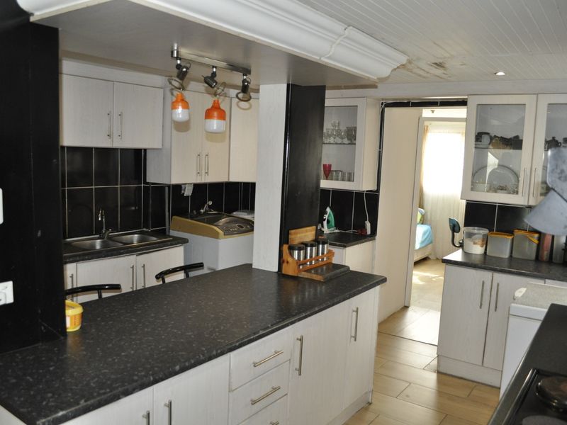 A functional kitchen featuring white cabinetry, dark countertops, tiled backsplash, and tiled flooring, with visible ceiling damage requiring maintenance.