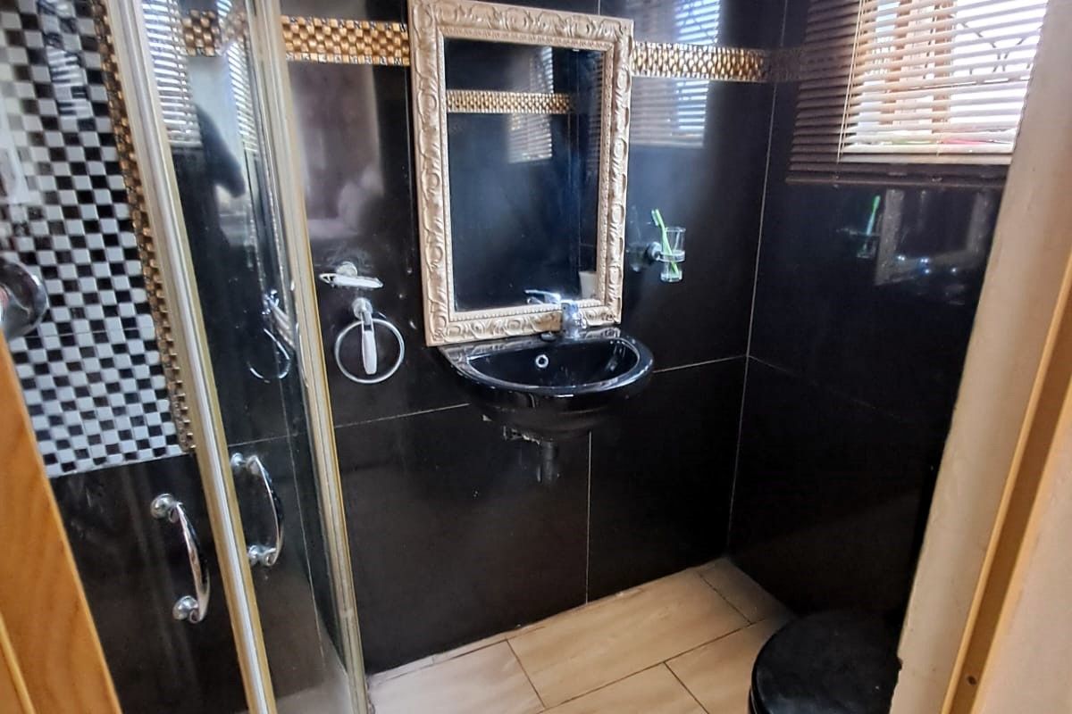 A compact bathroom featuring black wall tiles, a corner shower enclosure, a wall-mounted basin, and a toilet with wood-look floor tiling.